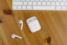 Close-up view of wireless earbuds next to an Apple keyboard on a wooden desk surface.