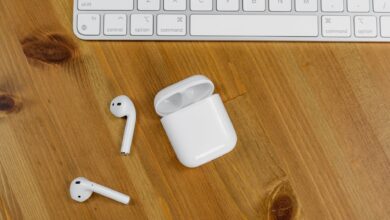 Close-up view of wireless earbuds next to an Apple keyboard on a wooden desk surface.