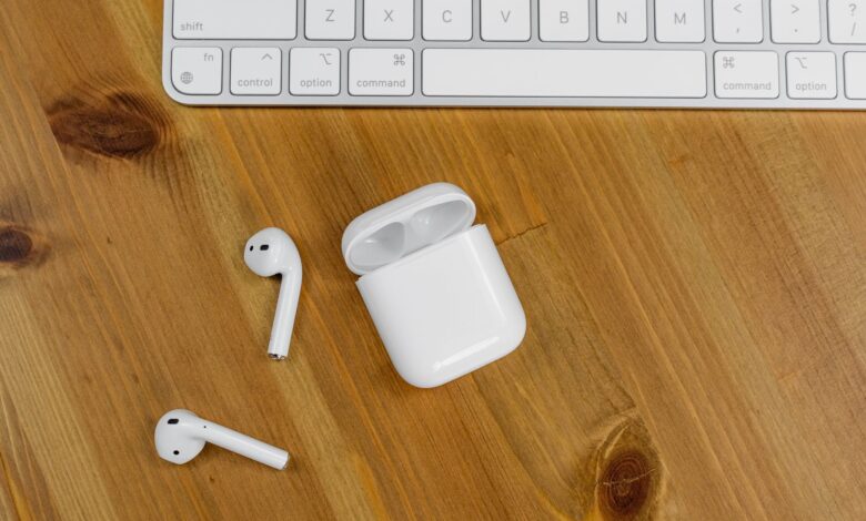 Close-up view of wireless earbuds next to an Apple keyboard on a wooden desk surface.