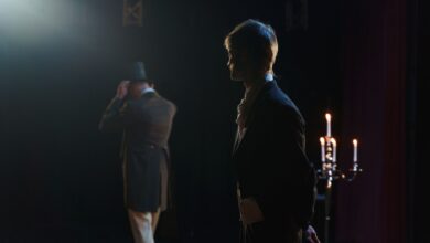 Two actors in Victorian costumes perform a dramatic scene on stage, lit by candlelight.