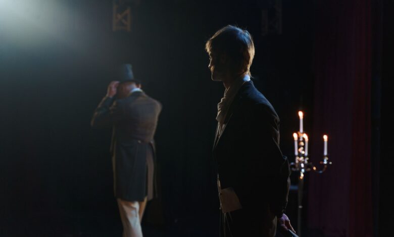 Two actors in Victorian costumes perform a dramatic scene on stage, lit by candlelight.