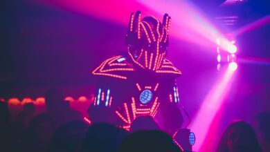 Anonymous person in illuminated futuristic costume of robot performing show on stage of modern nightclub with neon illumination
