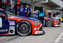 Close-up of colorful race cars in a pit stop with mechanics and crew preparing for a motorsport event.