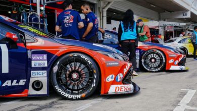 Close-up of colorful race cars in a pit stop with mechanics and crew preparing for a motorsport event.
