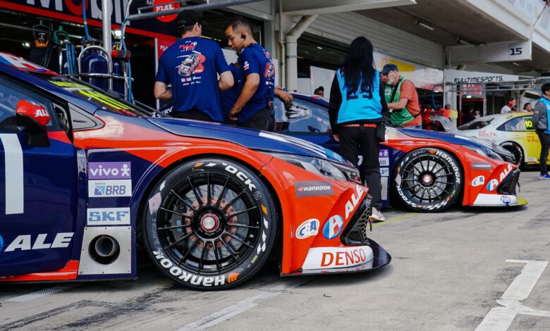 Close-up of colorful race cars in a pit stop with mechanics and crew preparing for a motorsport event.