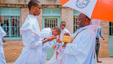 A priest providing communion to altar boys during an outdoor religious ceremony.