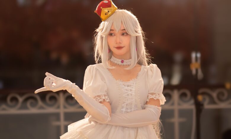 Cosplayer dressed as an elegant princess with white hair and gown, wearing a red crown.