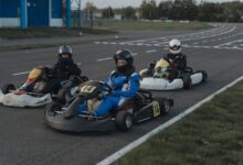 Three go-kart racers in protective gear sit ready on a racing track.