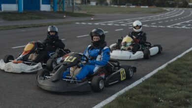 Three go-kart racers in protective gear sit ready on a racing track.