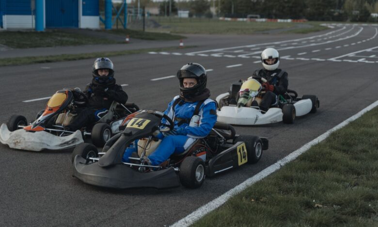 Three go-kart racers in protective gear sit ready on a racing track.