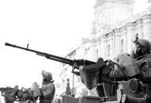 Monochrome image of soldiers in armored tanks, equipped with rifles, patrolling urban surroundings.