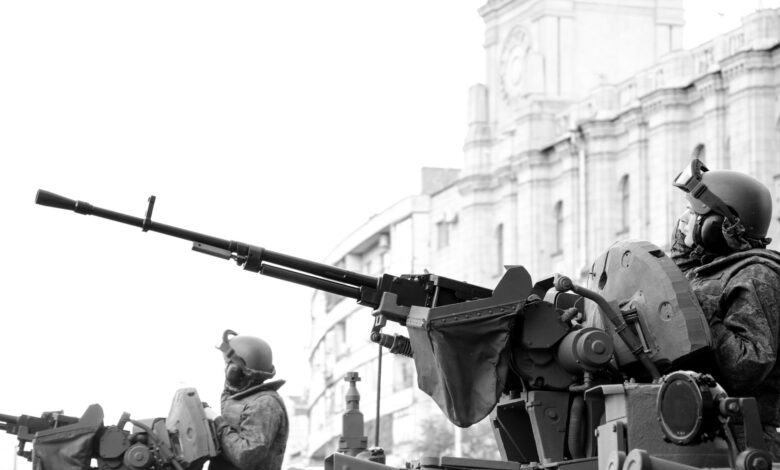 Monochrome image of soldiers in armored tanks, equipped with rifles, patrolling urban surroundings.