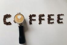 Artistic arrangement of coffee beans spelling 'coffee' with a portafilter and latte art heart.