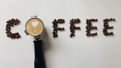 Artistic arrangement of coffee beans spelling 'coffee' with a portafilter and latte art heart.