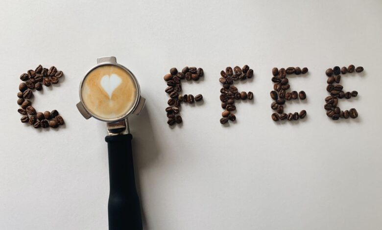 Artistic arrangement of coffee beans spelling 'coffee' with a portafilter and latte art heart.