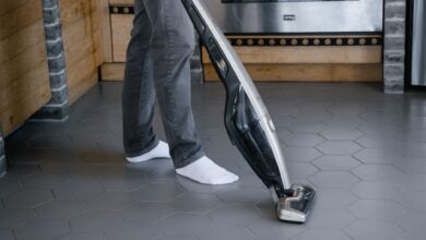 A person cleaning a tiled floor with a modern vacuum cleaner indoors.
