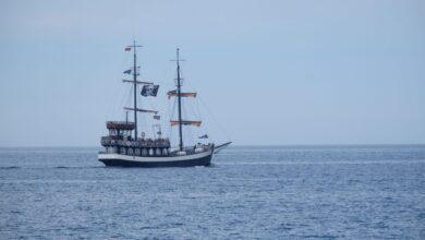 A vintage pirate ship with sails unfolds on calm ocean waters under a clear sky.
