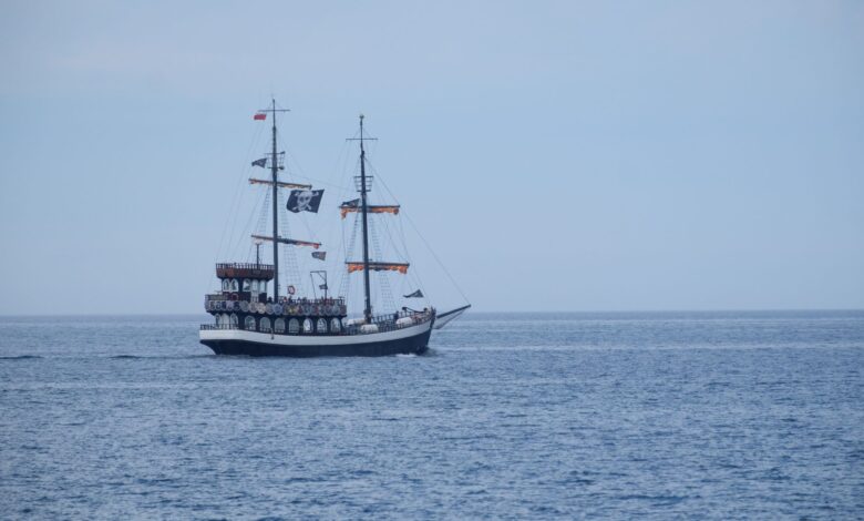 A vintage pirate ship with sails unfolds on calm ocean waters under a clear sky.