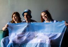 Three people holding the Argentine flag indoors. Celebratory and patriotic mood.