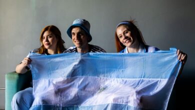 Three people holding the Argentine flag indoors. Celebratory and patriotic mood.
