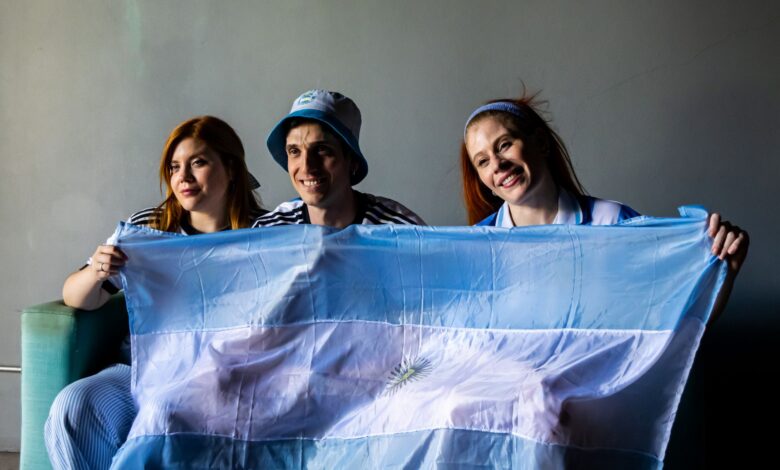 Three people holding the Argentine flag indoors. Celebratory and patriotic mood.