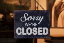 A 'Sorry We're Closed' sign hangs in a shop window, indicating closure.