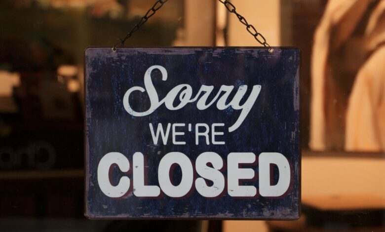 A 'Sorry We're Closed' sign hangs in a shop window, indicating closure.