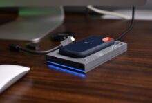 A close-up view of a portable USB SSD placed on a wooden desk with connected cables.