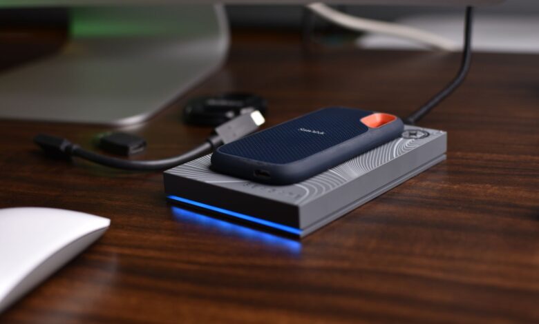 A close-up view of a portable USB SSD placed on a wooden desk with connected cables.