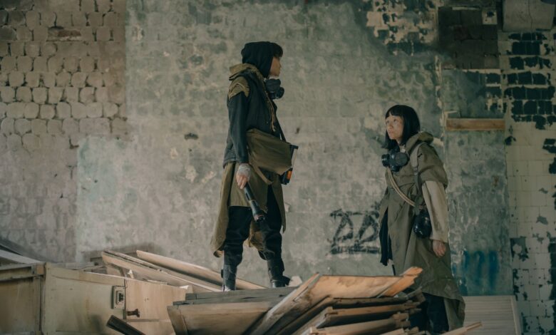 Two people in urban survival gear explore a dystopian, abandoned building setting.