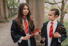 Two girls dressed as young wizards with spell books and wands in an outdoor setting.