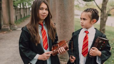 Two girls dressed as young wizards with spell books and wands in an outdoor setting.