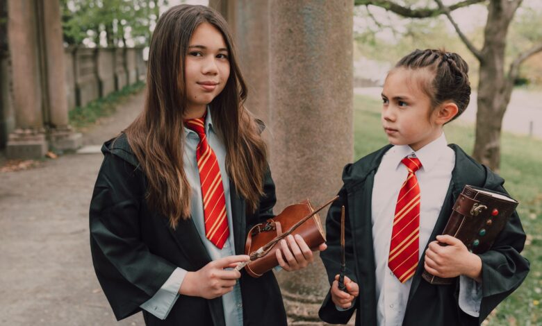 Two girls dressed as young wizards with spell books and wands in an outdoor setting.
