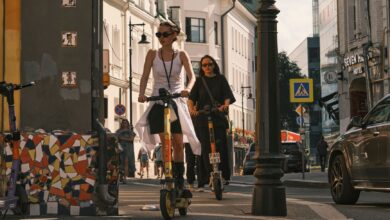Two women riding electric scooters on a city street, showcasing urban commute.