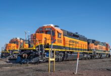 Three bright orange BNSF locomotives parked on railroad tracks under a clear blue sky.