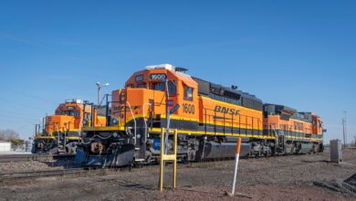 Three bright orange BNSF locomotives parked on railroad tracks under a clear blue sky.
