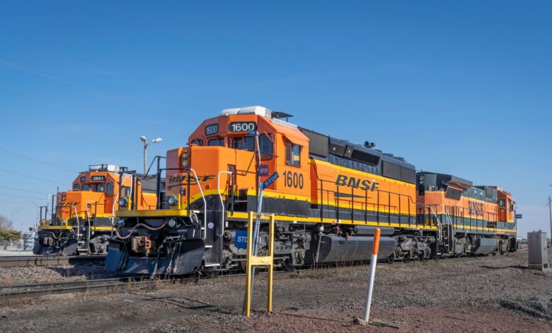 Three bright orange BNSF locomotives parked on railroad tracks under a clear blue sky.
