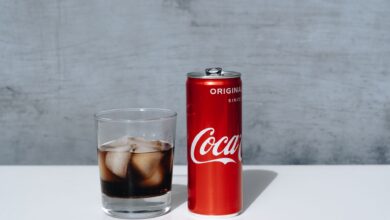 Chilled Coca-Cola can and drink with ice cubes in glass on minimalistic surface.