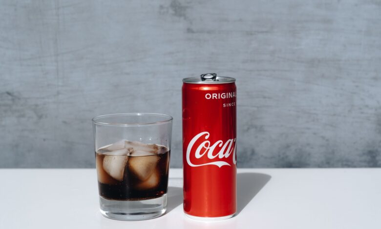 Chilled Coca-Cola can and drink with ice cubes in glass on minimalistic surface.
