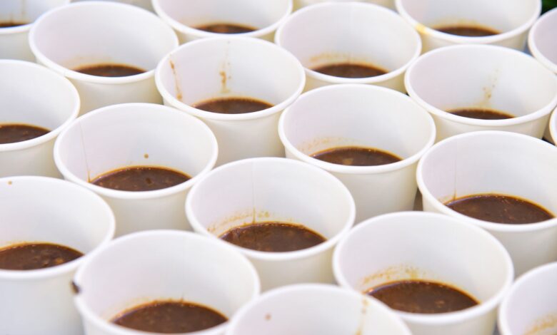 Close-up of multiple white paper cups containing brown liquid, arranged uniformly.
