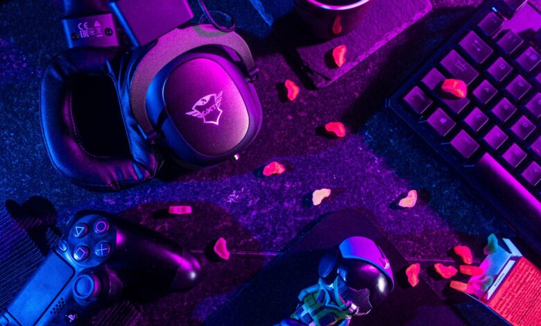 Colorful flat lay of gaming gear including headset, controller, and keyboard under vibrant lighting.