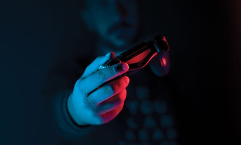 Close-up of a man's hand holding a joystick against a dark background with red and blue lighting.