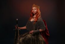 Portrait of a regal woman wearing a crown and holding a sword against a dark background.