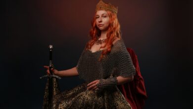 Portrait of a regal woman wearing a crown and holding a sword against a dark background.