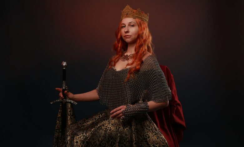 Portrait of a regal woman wearing a crown and holding a sword against a dark background.