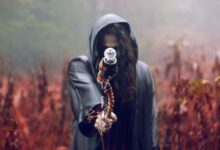 A hooded figure holds a staff in a misty, autumn forest setting, evoking mystery and fantasy.