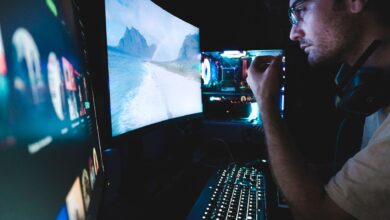 A man in eyeglasses focused on multiple screens, showcasing modern technology setup.