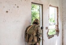 Airsoft player in camouflage navigating through a deserted, partially destroyed building.