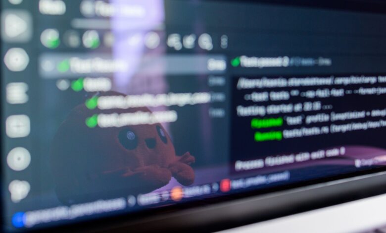 Close-up of a laptop screen displaying programming code with a cute plush toy reflecting.