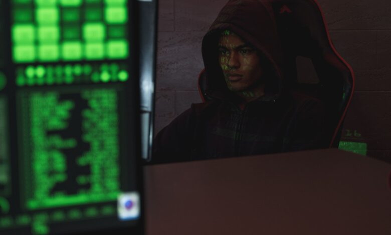 Hooded programmer intensely focused on computer screen, ensuring data protection and cyber security.